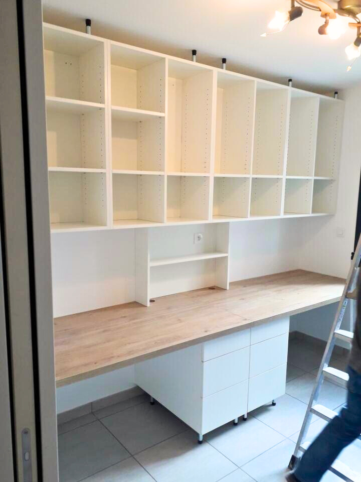 Espace de travail avec des étagères blanches au mur et un bureau en bois.