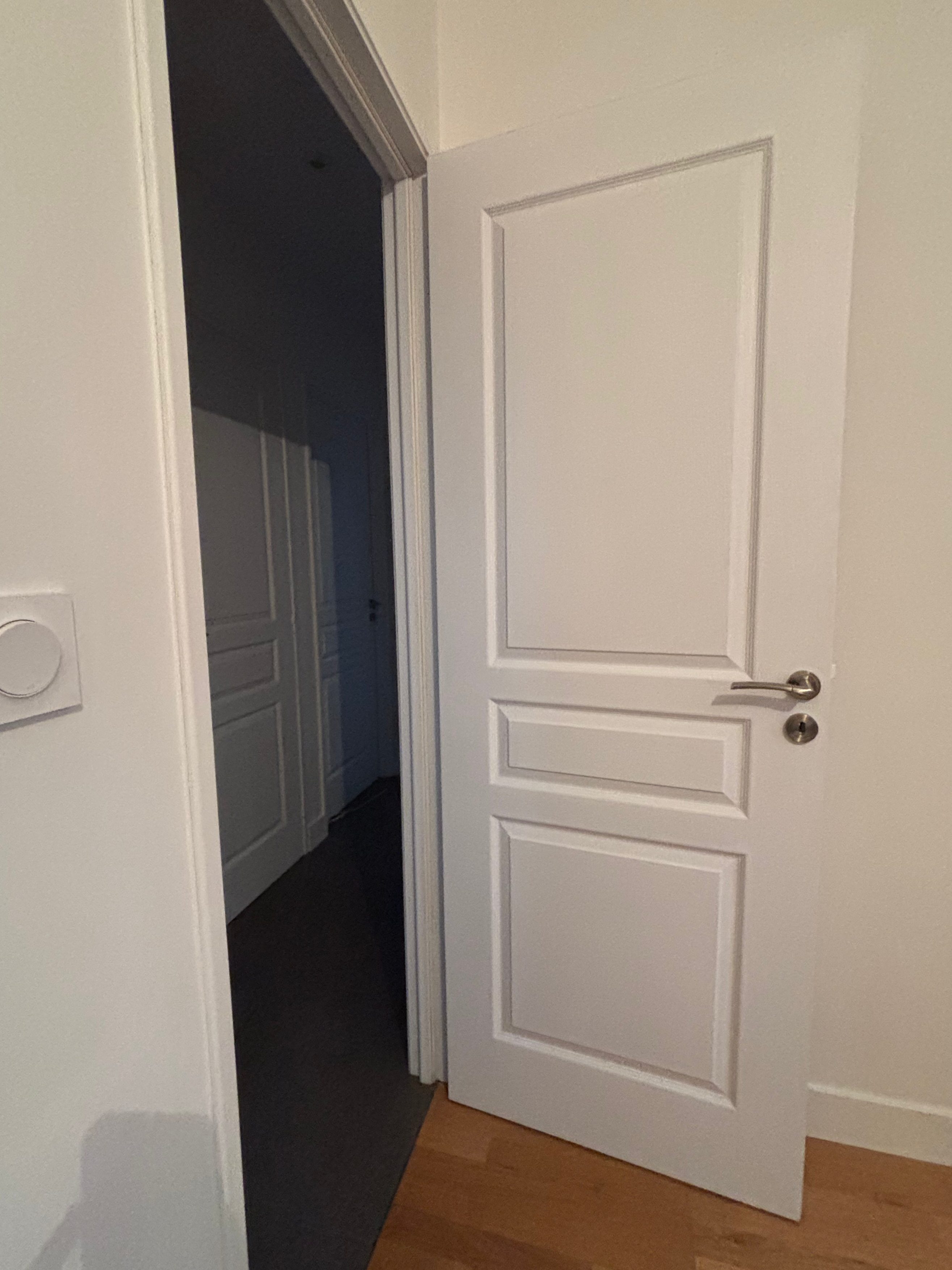 Une porte blanche entrouverte donnant sur un couloir.