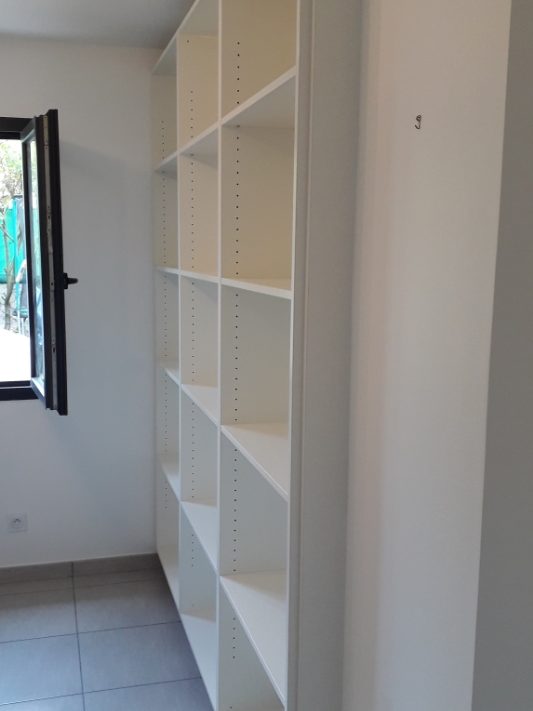 Une pièce avec des étagères blanches vides et une fenêtre ouverte.